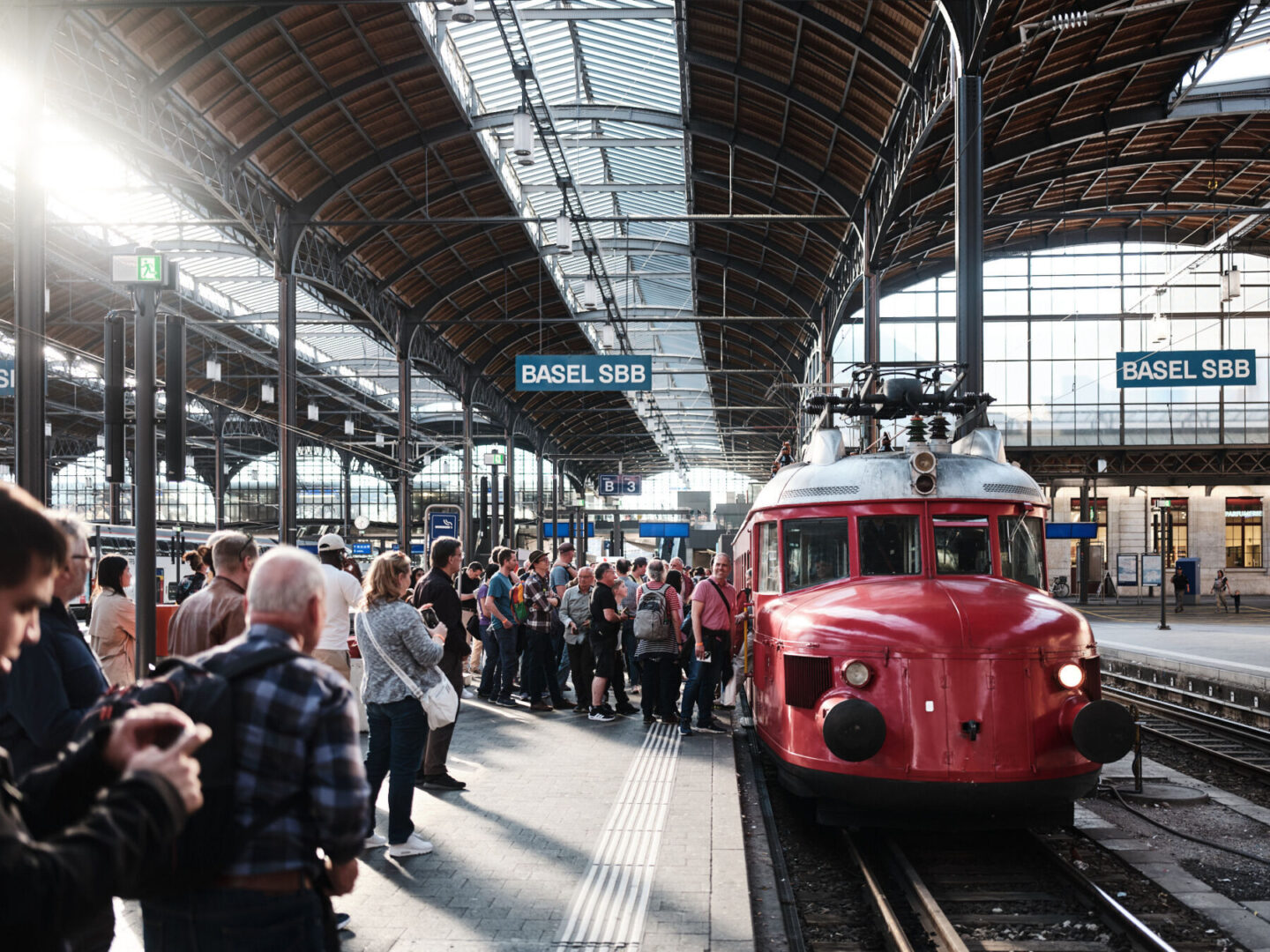 Roter historischer Zug am Bahnhof Basel SBB, umringt von einer Gruppe wartender Menschen.