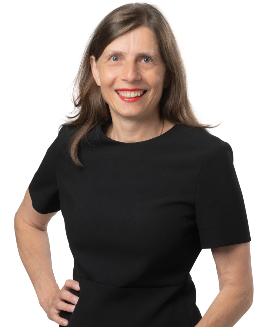 Bettina Balmer Porträt einer lächelnden Frau mit braunen Haaren in einem schwarzen Kleid vor weissem Hintergrund.