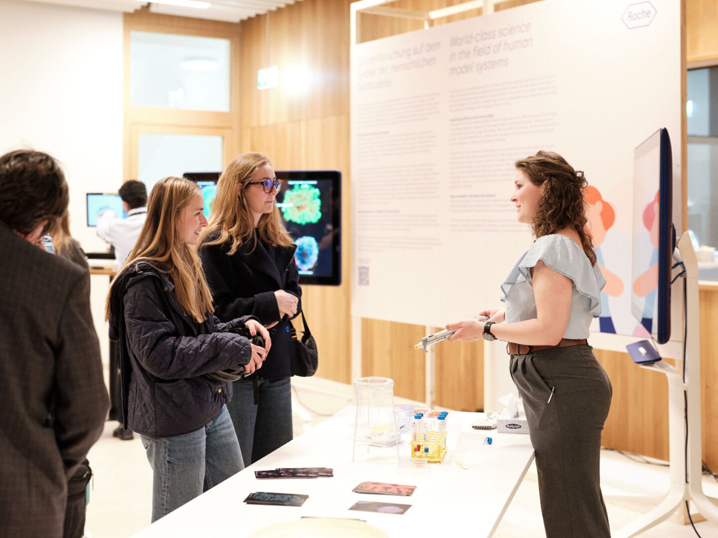 250509 IN25 Finals 0082 Web Res Samuel Bramley Eine Frau erklärt einer Gruppe junger Frauen an einem Informationstisch die Inhalte eines Posters.