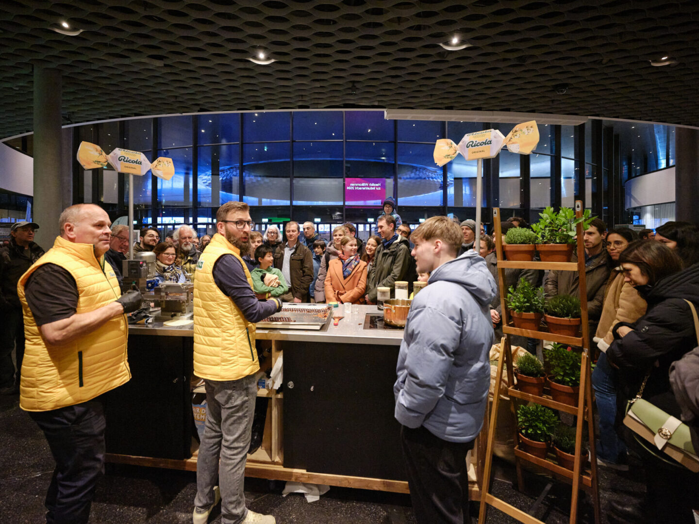 INRB24 Foto Samuel Bramley klein 149 Zwei Mitarbeiter in gelben Westen bedienen Kunden an einem Ricoala-Kaffeestand.
